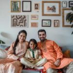 Smiling family of three in traditional clothing sitting on sofa indoors, embodying togetherness.